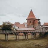 Castel gotic cu turnuri ascuțite și un pod lung de lemn, așezat pe o stâncă deasupra unui pârâu