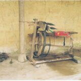 Roată de tors cu lână într-o cameră veche de casă țărănească, luminată de o lampă caldă